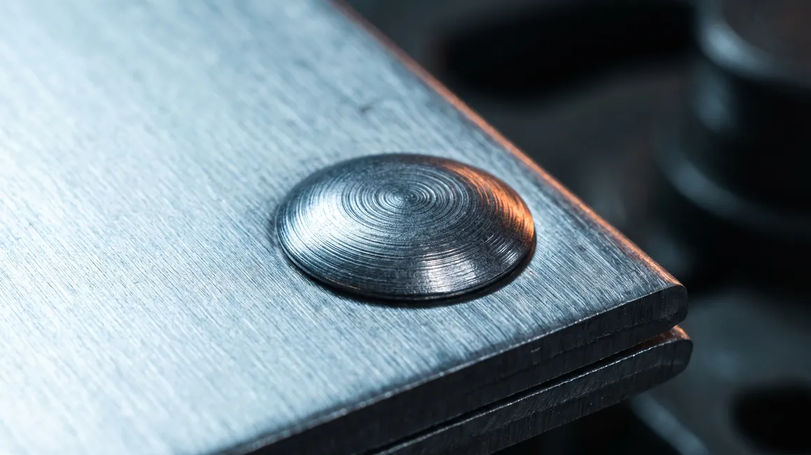 Macro detail of a formed rivet head in brushed steel showing concentric tool marks.