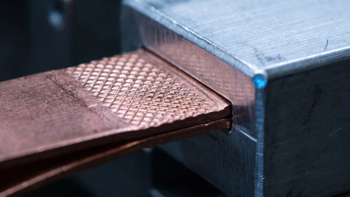 Macro detail of an ultrasonic weld between a copper tab and an aluminum busbar, showing the knurled joint pattern.