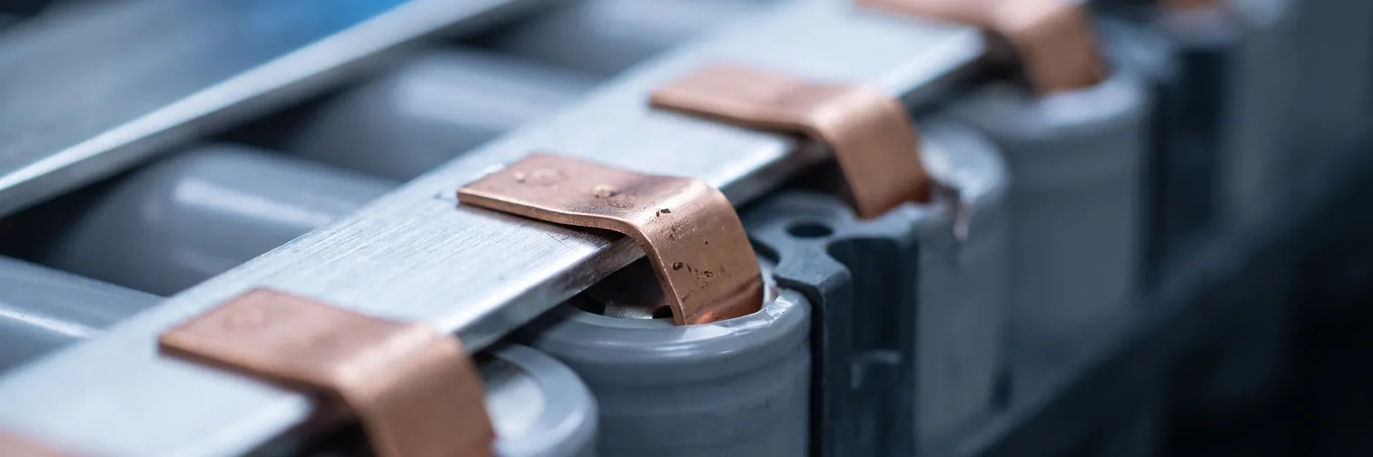 A lithium battery module under assembly, copper tabs folded over an aluminum busbar above a row of cells.