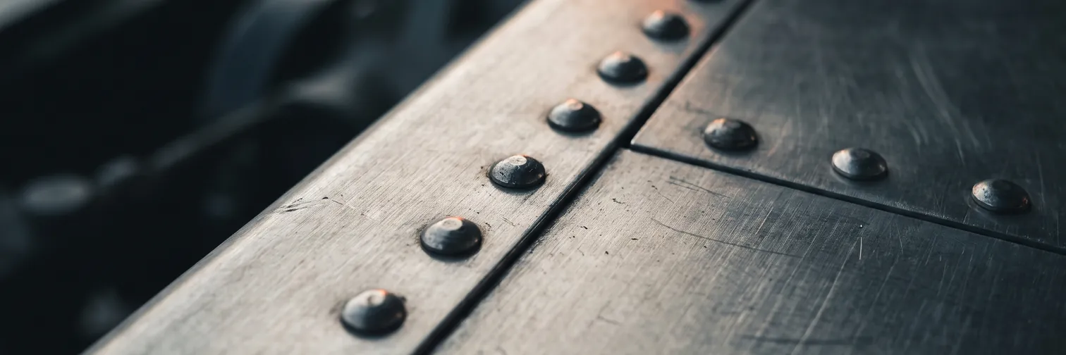Two brushed aluminum structural panels joined along a seam by a row of evenly spaced formed rivets.