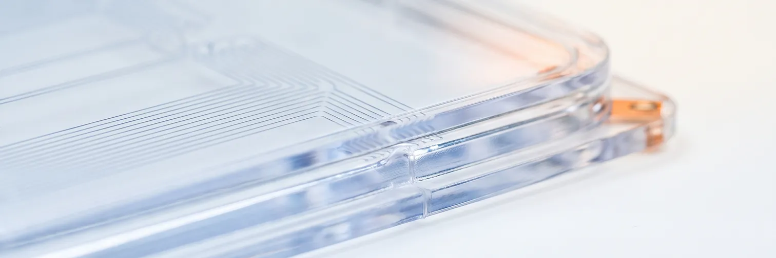 A clear medical polymer cartridge on a white surface, fine internal channels visible through the body.