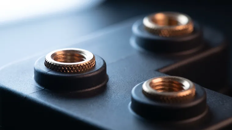 A black moulded polymer part with knurled brass threaded inserts set flush into its bosses.