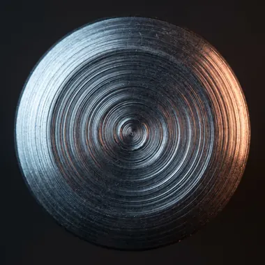 A rivet head formed by an orbital path, showing smooth continuous circular tooling marks.