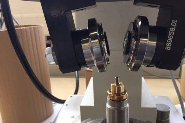 A roller forming head running a rolled edge onto a brass component.