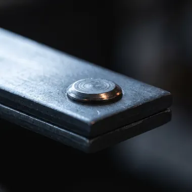 A precisely formed rivet seated flush in a stack of two steel plates.